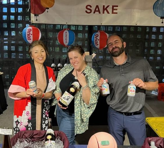 A group of three E-Corp Sales reps standing with bottles in their hand, pouring at the SushiDen Rooftop party in 2024.